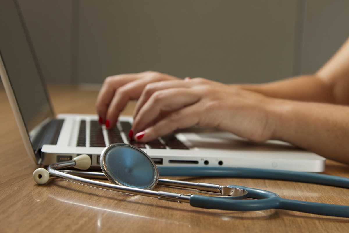 Clinician using a laptop with stethoscope on desk